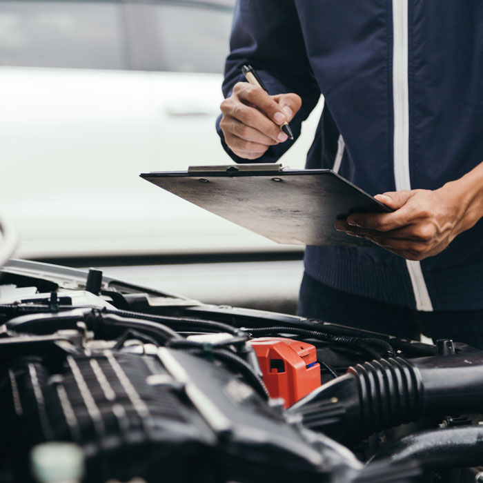 mechanic with checklist looking under hood of car
